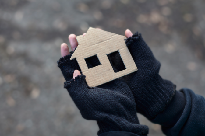 Unhoused neighbor holding a cardboard cutout in the shape of a house